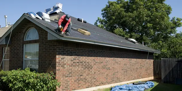 A roofer kneeling on the roof of a brick house on a sunny day